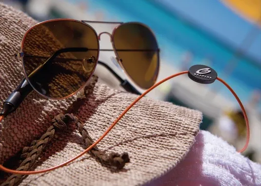 GRAPLRZ retainer holding a pair of aviator sunglasses on a beach towel