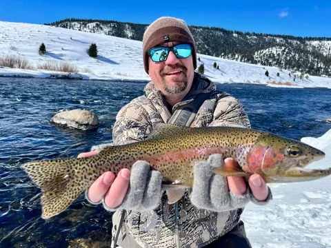 Cordell holding a cutthroat trout on a snowy riverbank in winter